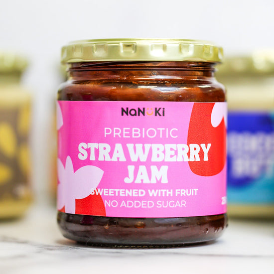 A jar of Nan Ki Prebiotic Strawberry Jam on a light marble surface with a soft-focus background showing other jars.