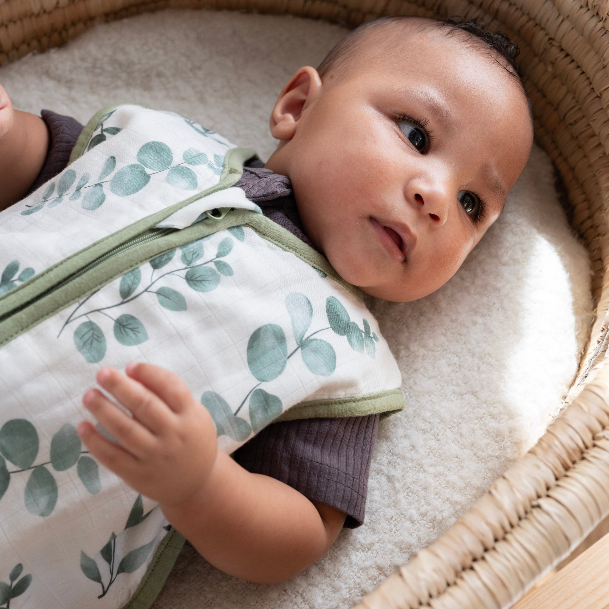 Baby wrapped in a green and white swaddle in a wicker crib.