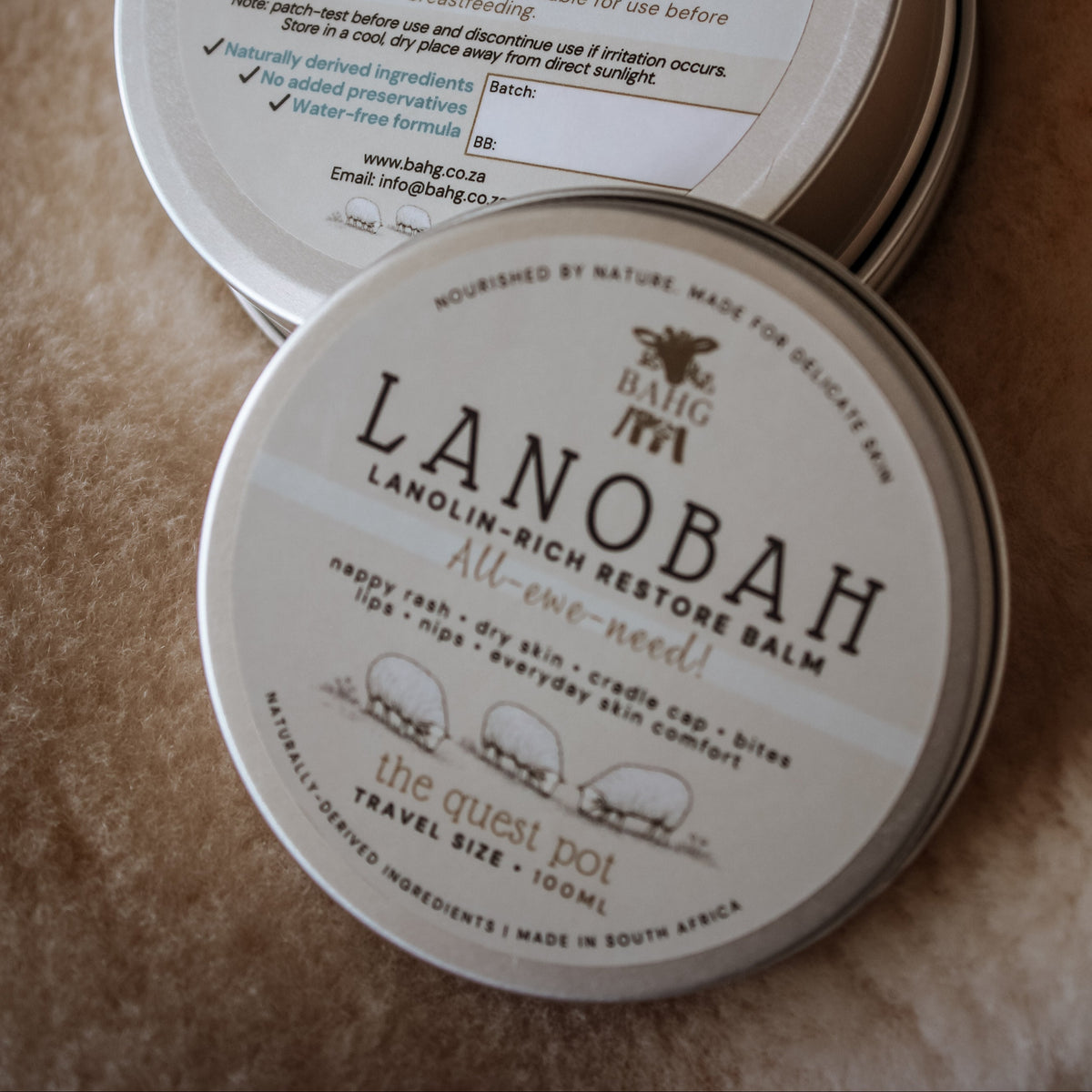 Two tins of Lanobah balm on a textured surface
