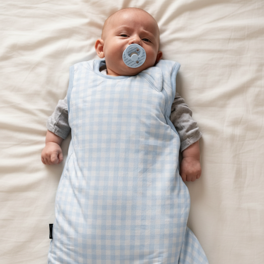 Baby in a blue checkered sleep bag with a pacifier on a dark background