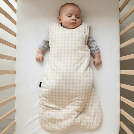 Baby lying on a black surface wearing a beige checkered sleep bag.