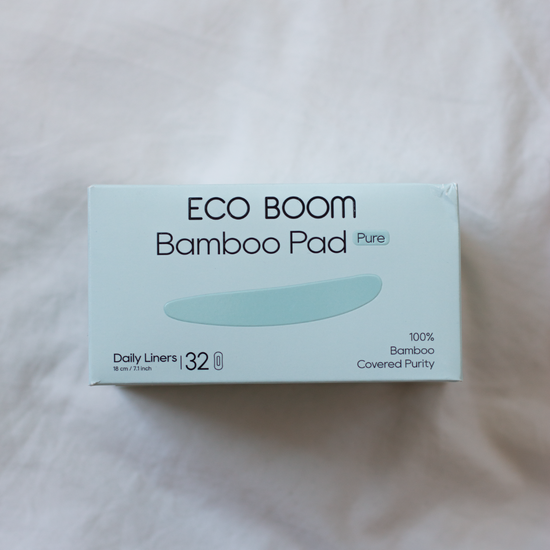 A box of ECO BOOM Bamboo Pad Pure daily liners, size 32, resting on a soft, light-colored fabric background.