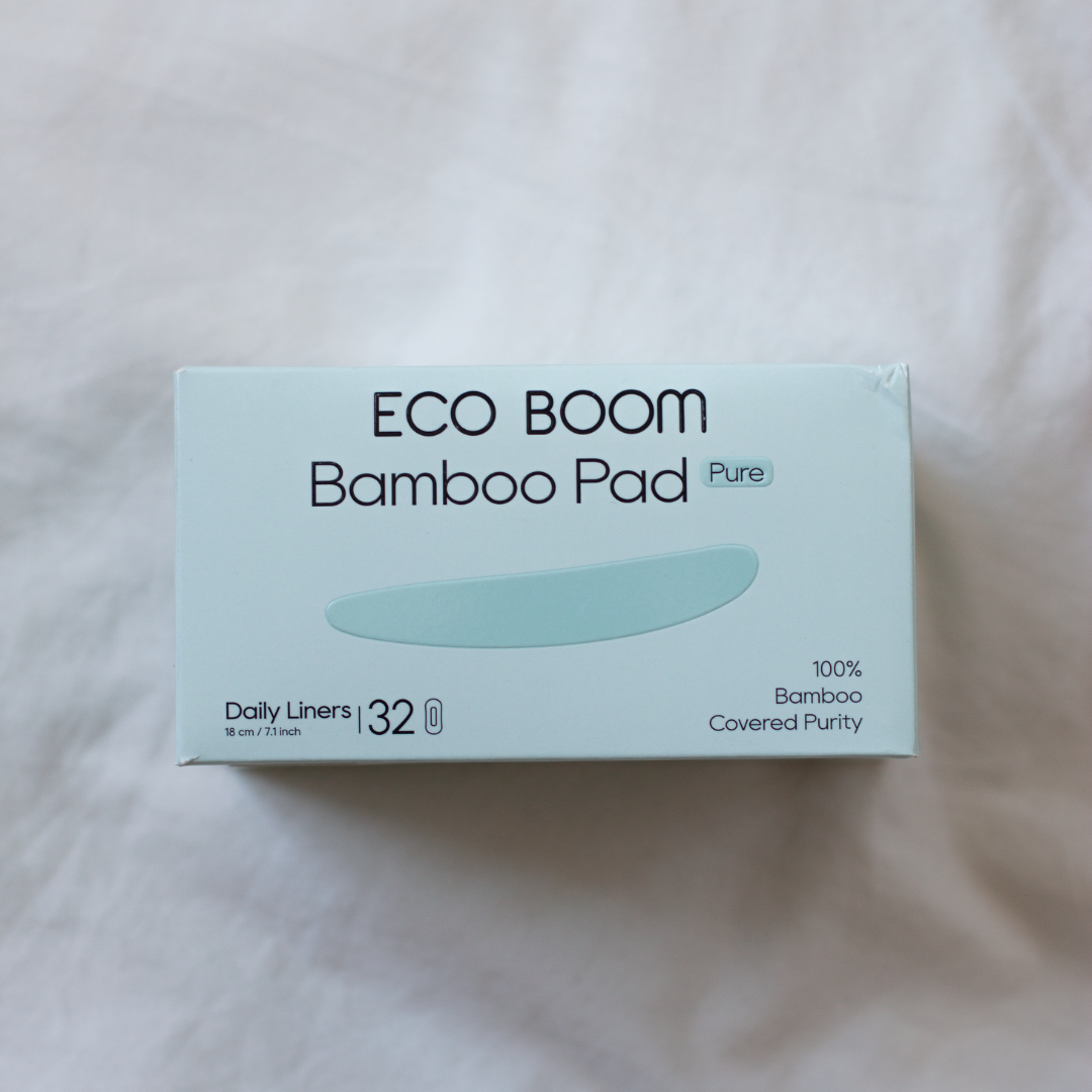 A box of ECO BOOM Bamboo Pad Pure daily liners, size 32, resting on a soft, light-colored fabric background.
