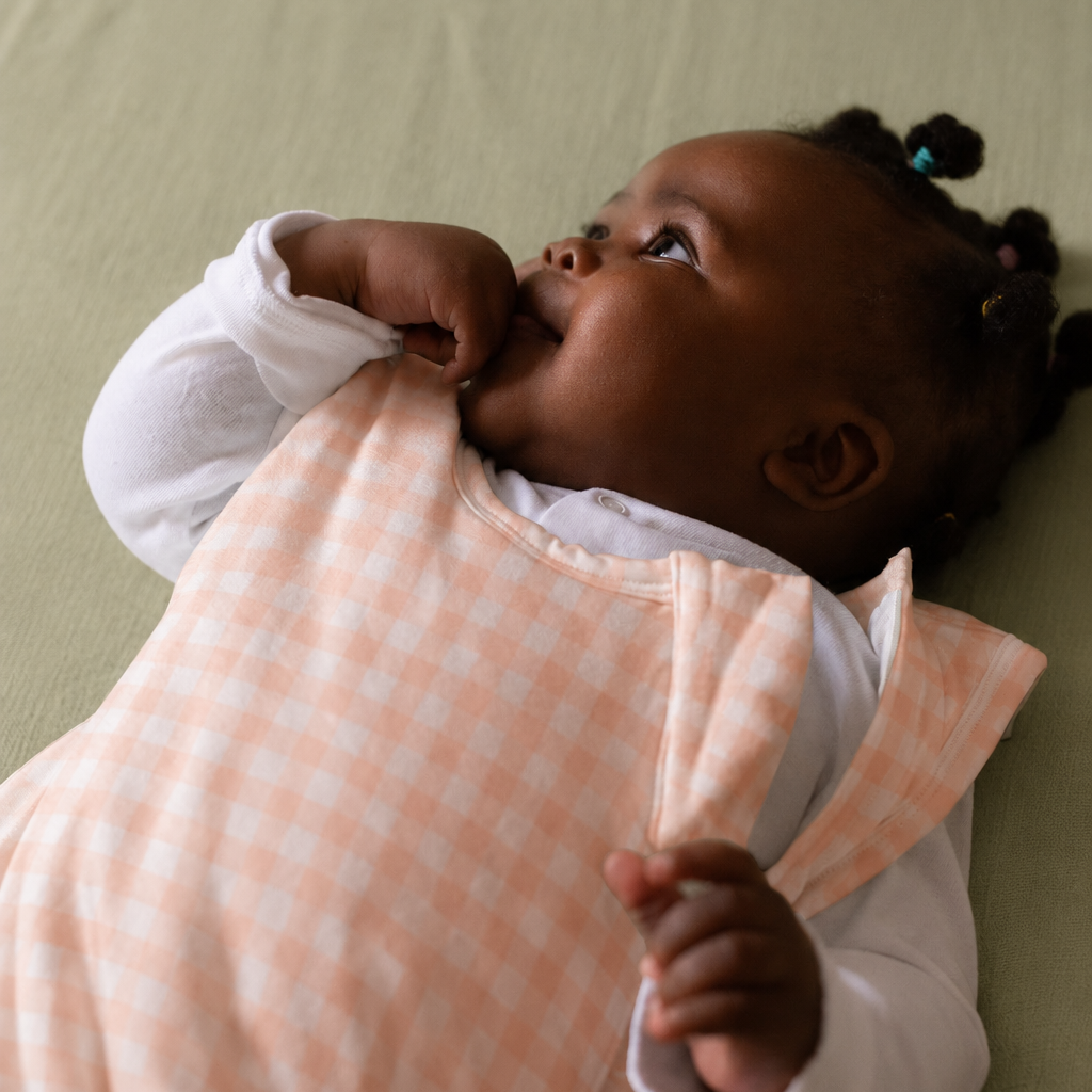 Baby wearing a peach and white checkered outfit lying on a green surface