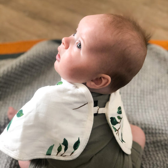 Baby wearing a bib with green leaf patterns on a textured surface