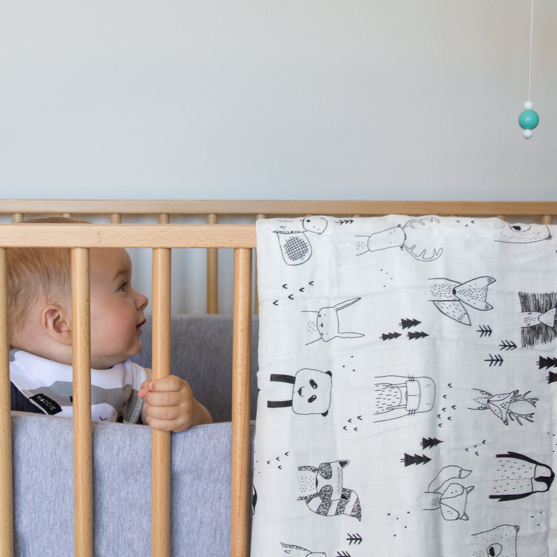Baby in a crib with a patterned blanket and mobile in a nursery