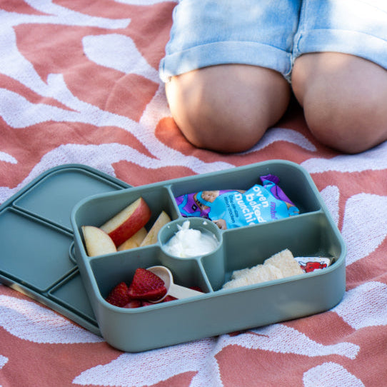 Children sitting on a patterned blanket with bento boxes containing snacks.