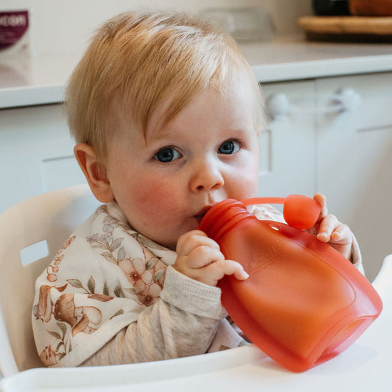 Baby in a high chair drinking from a red sippy cup in a kitchen setting