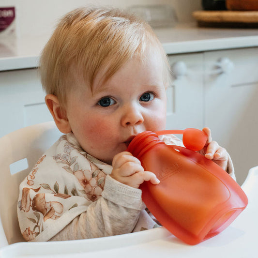 Baby in a high chair drinking from a red sippy cup in a kitchen setting
