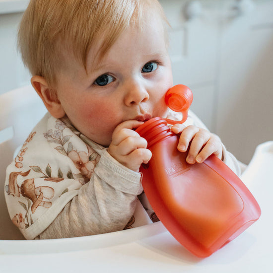 Baby drinking from a red sippy cup in a kitchen setting
