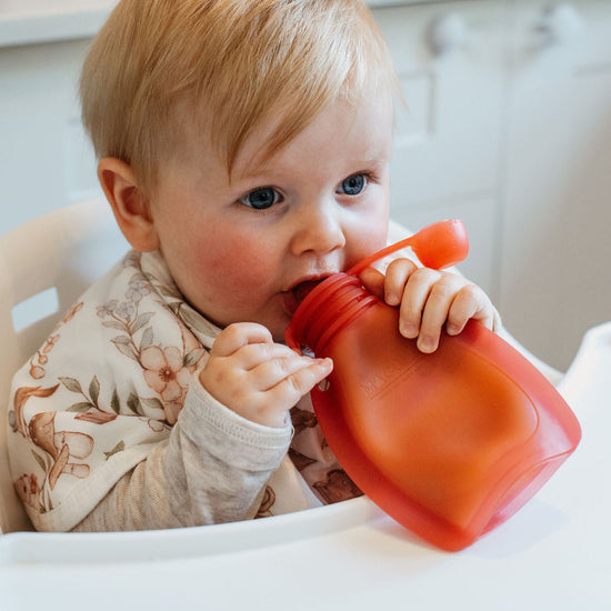Baby drinking from a red sippy cup in a kitchen setting