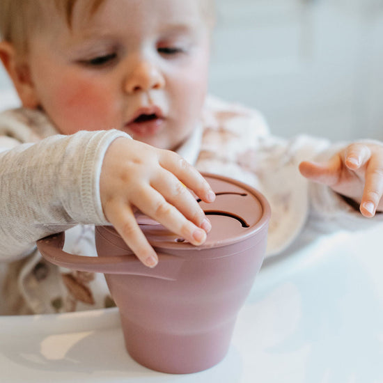 Child interacting with a pink silicone cup on a high chair