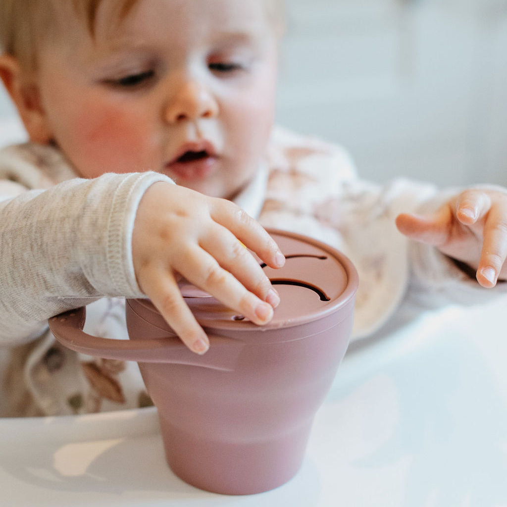 Child interacting with a pink silicone cup on a high chair