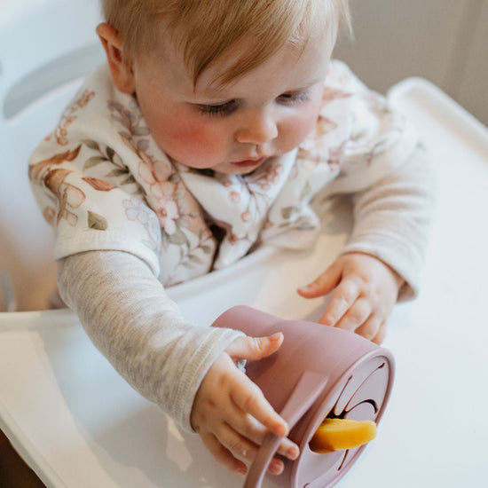 Child in a high chair holding a pink toy with a yellow top.