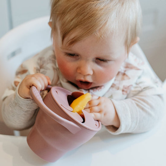 Baby in a high chair eating from a pink bowl