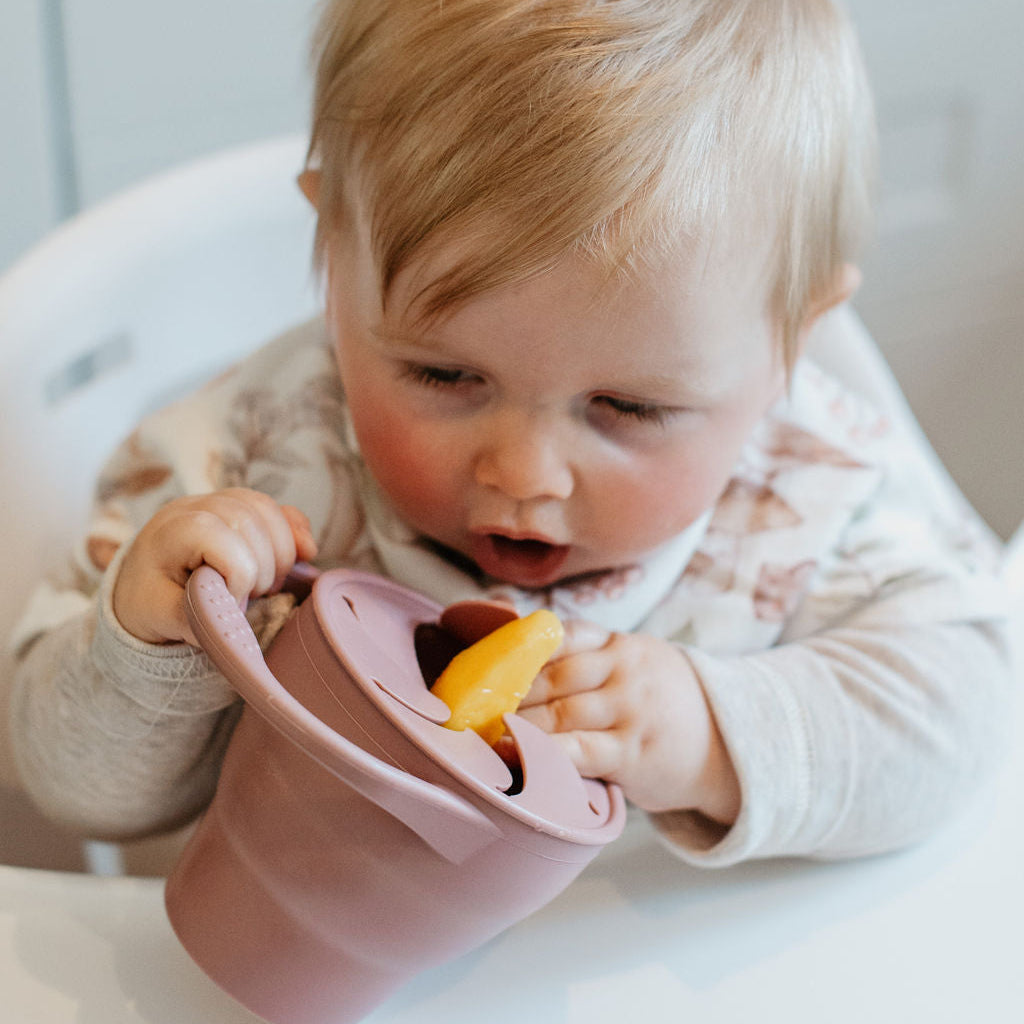 Baby in a high chair eating from a pink bowl