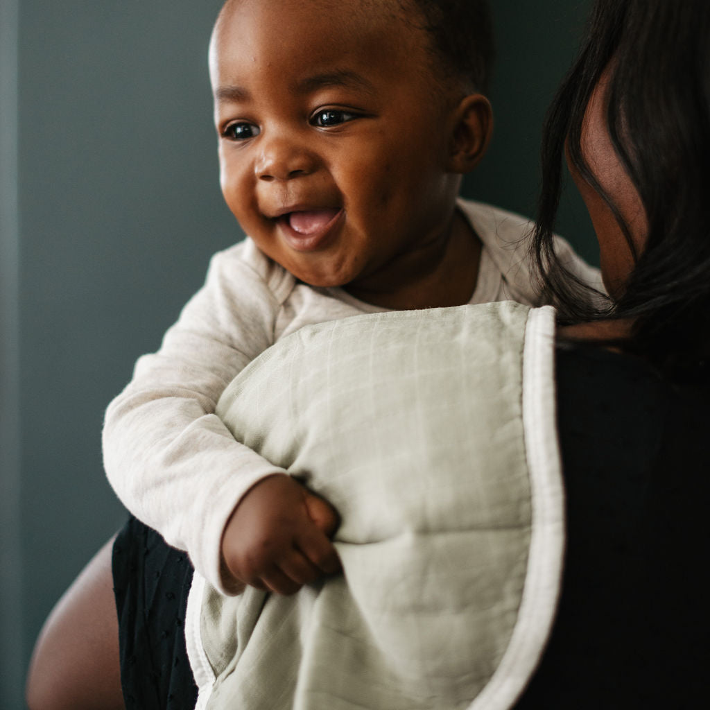 Baby wearing a white bib being held by an adult against a dark background