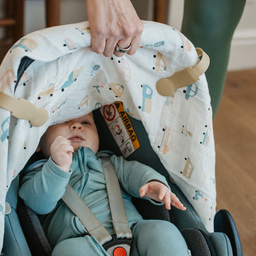 Baby in a car seat with a patterned cover, wearing a light blue outfit.