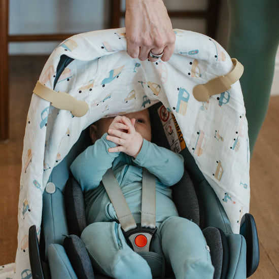 Child in a blue car seat with a patterned cover, held by an adult.