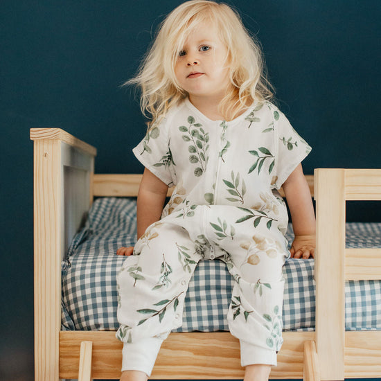 Child sitting on a small bed with a floral pattern against a dark blue wall.