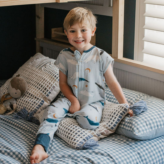 Child sitting on a bed with checkered bedding and pillows in a bedroom setting.