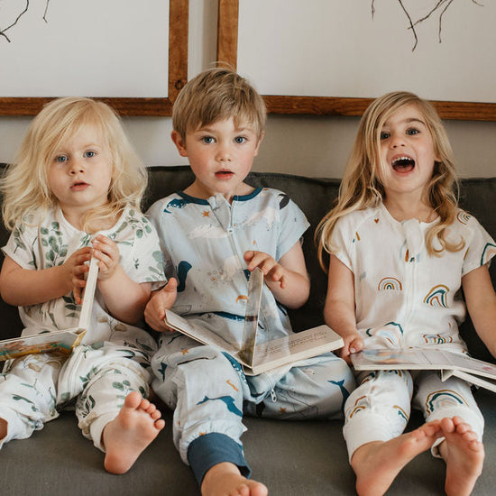 Three children in matching pajamas sitting on a couch with books.