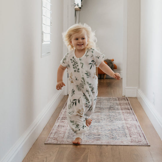 Child in a floral onesie running down a hallway with a rug