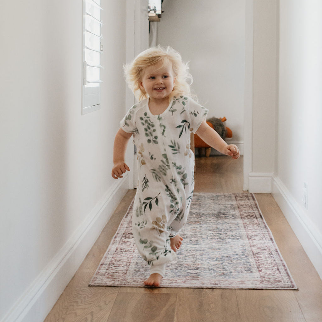 Child in a floral onesie running down a hallway with a rug