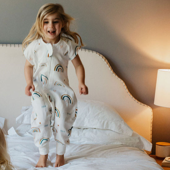 Two children in pajamas jumping on a bed in a bedroom.