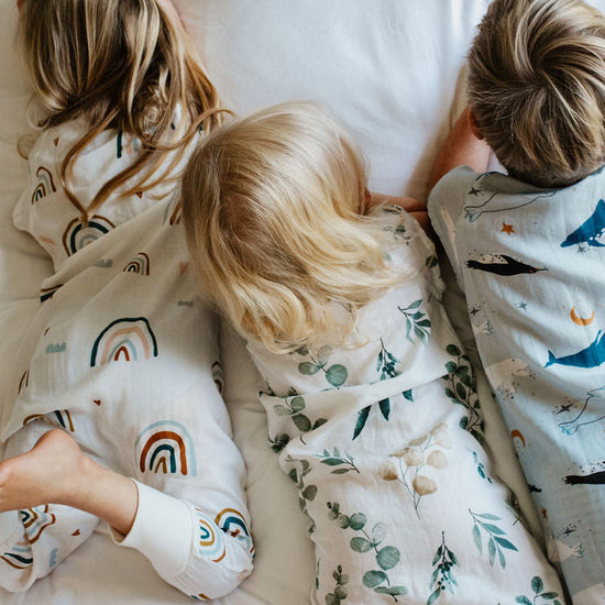 Three children in pajamas with animal patterns lying on a bed.