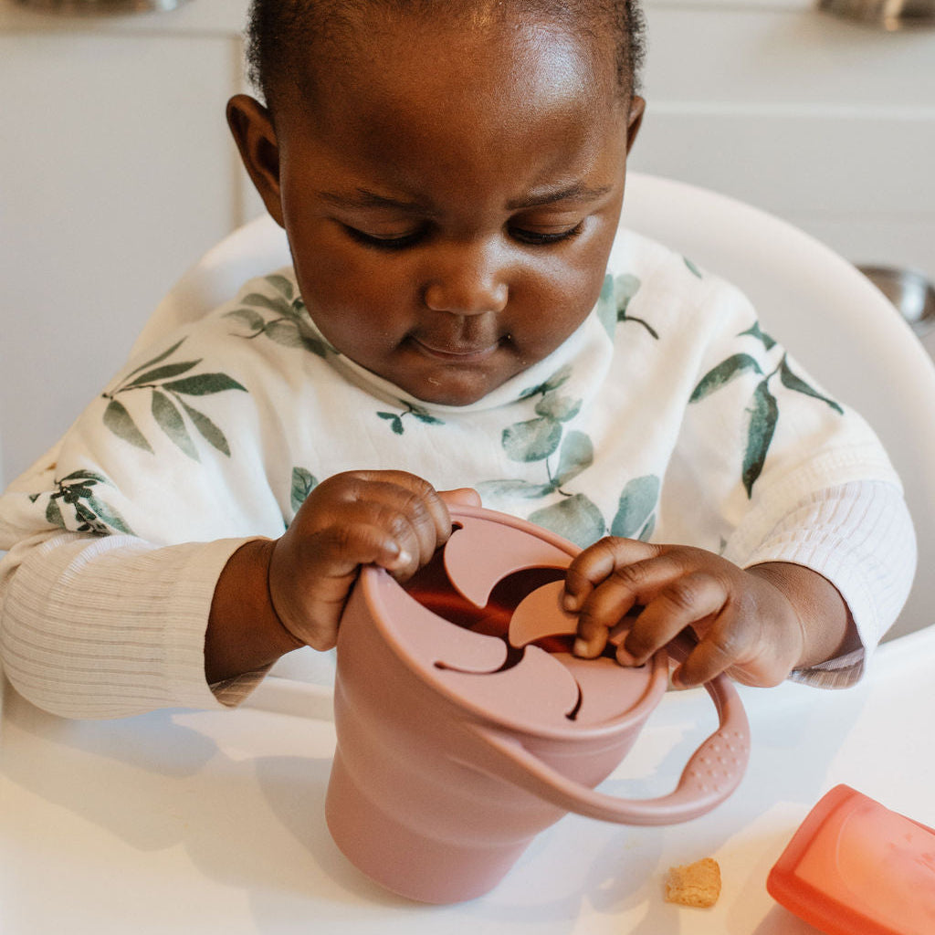 Child sitting in a high chair with a pink sippy cup in a kitchen setting