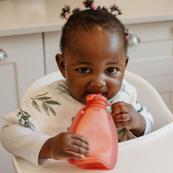Child holding a pink sippy cup in a kitchen setting