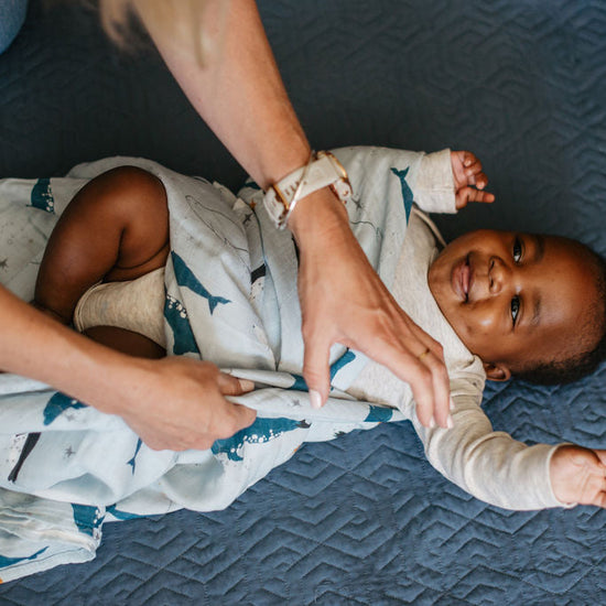 Baby lying on a blue textured surface with a person adjusting a blanket