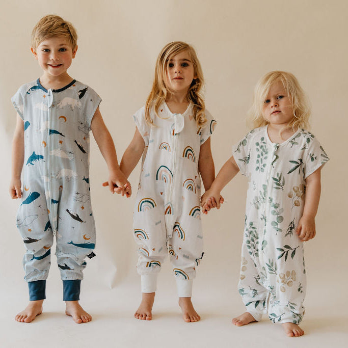 Three children holding hands wearing patterned onesies on a plain background