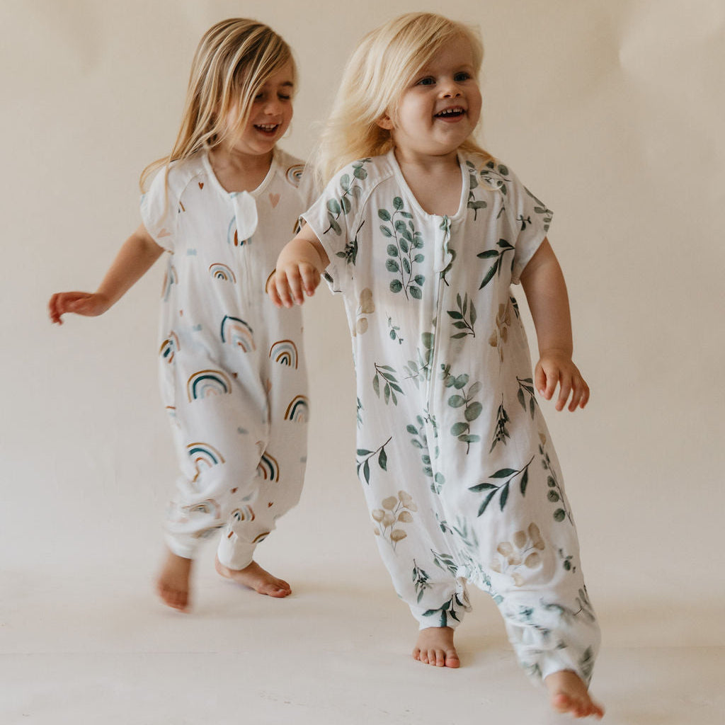 Two children wearing floral and rainbow-patterned onesies on a plain background