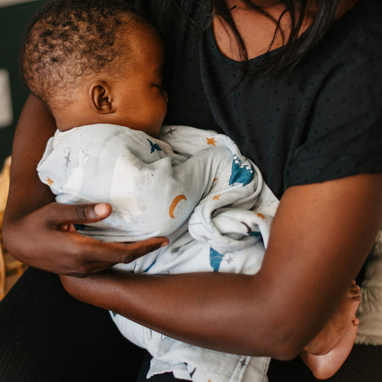 Woman holding a baby wrapped in a white blanket with colorful patterns.