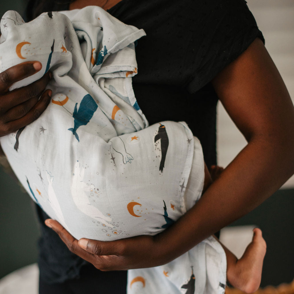 Person holding a baby swaddled in a blanket with animal prints.