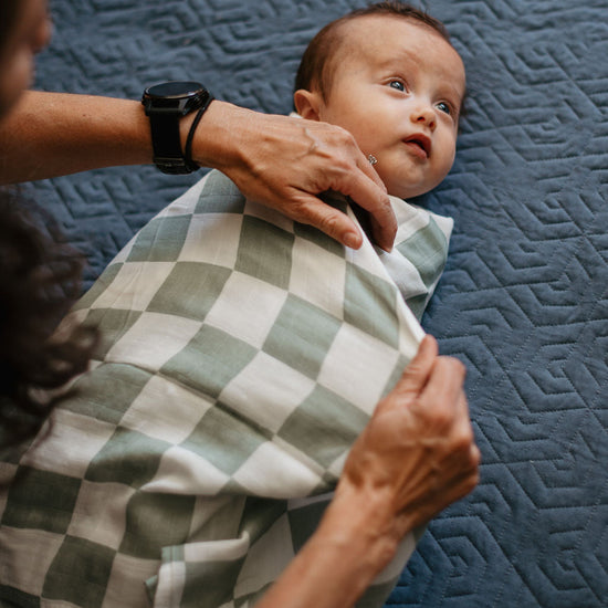 Baby being swaddled with a checkered blanket on a textured blue surface