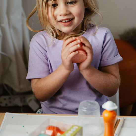 Young girl holding a pink object at a table with various items