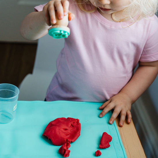 Child playing with red play dough on a blue table