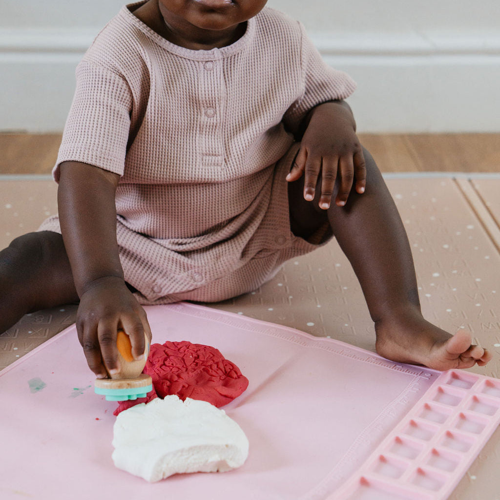 Child playing with play dough on a pink mat