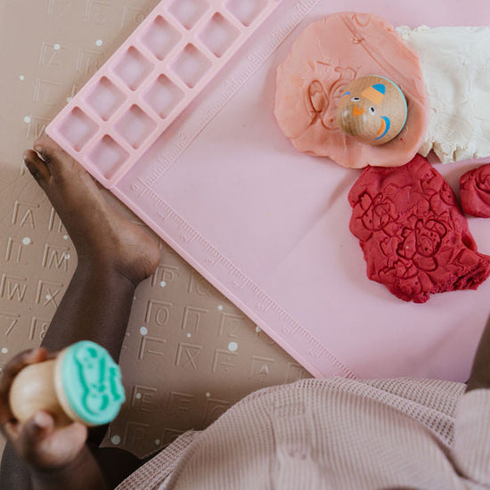 Pink silicone mold tray with colorful play dough on a textured surface