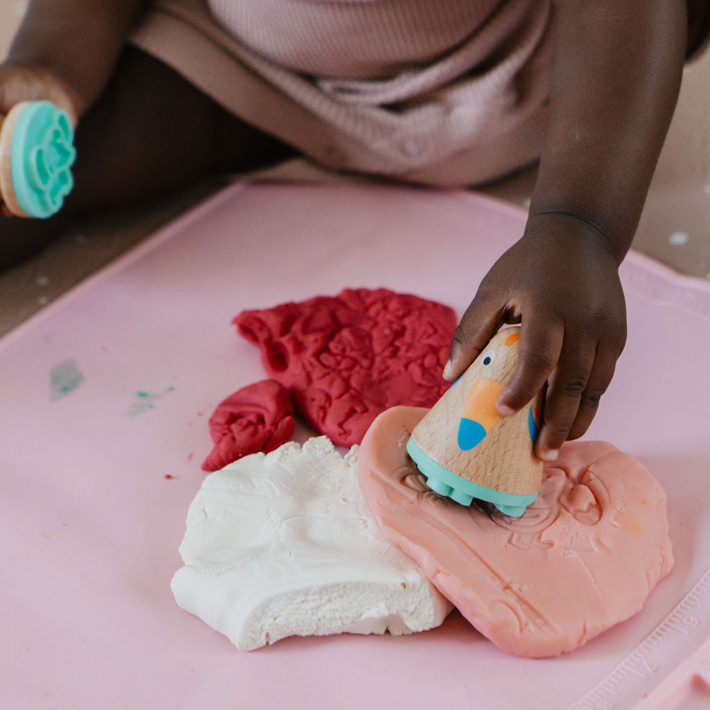 Child playing with colorful play dough on a pink surface