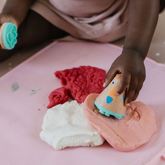 Child playing with colorful play dough on a pink surface
