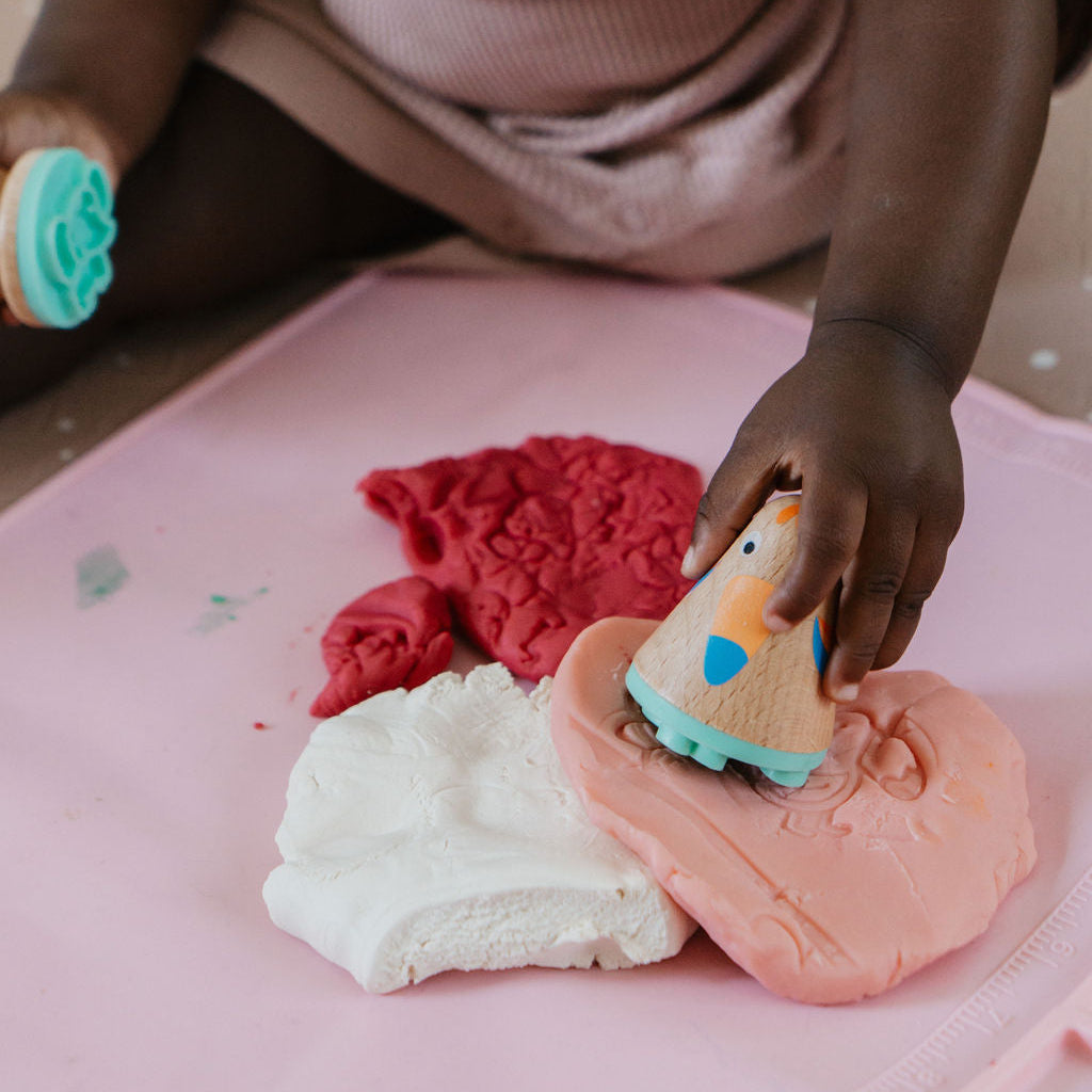 Child playing with colorful play dough on a pink surface