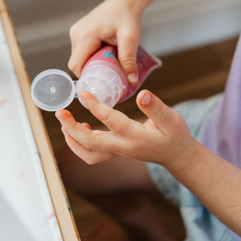 Child applying hand sanitizer from a pink bottle with a pump.