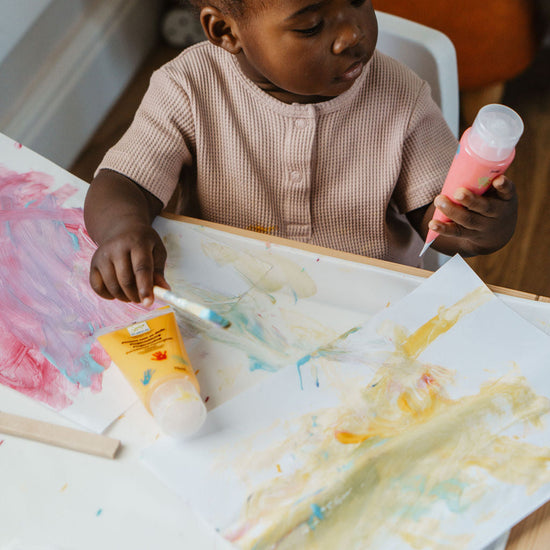 Child painting with a brush and colorful paint on a table.