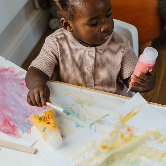 Child painting with a brush and colorful paint on a table.