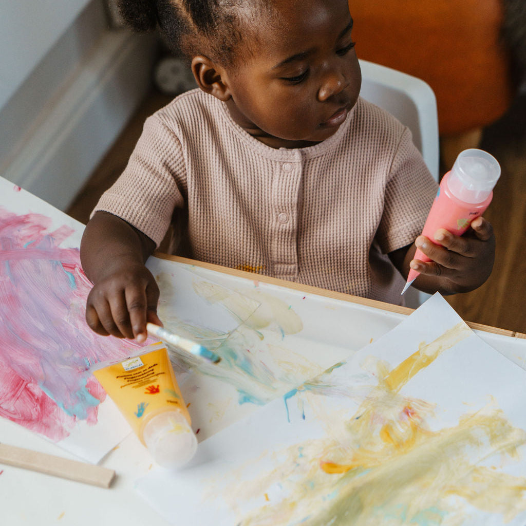 Child painting with a brush and colorful paint on a table.