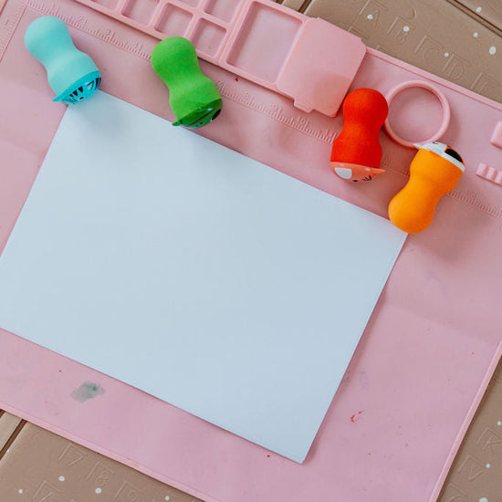 Colorful paper clips on a pink cutting mat with a white sheet of paper.